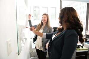 Zwei Personen planen gemeinsam an einem Whiteboard, lachen und tauschen sich in einem modernen Büro aus.