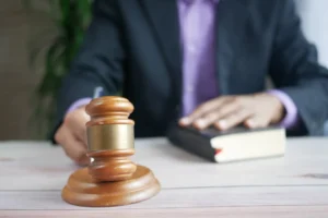Eine Person im Anzug schlägt mit einem Richterhammer auf den Tisch, daneben liegt ein Gesetzbuch – Darstellung von Recht und Ordnung.