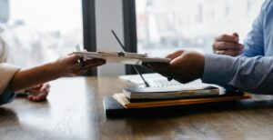 Zwei Personen reichen sich ein Klemmbrett mit Dokumenten über einen Tisch hinweg in einem modernen Büro.