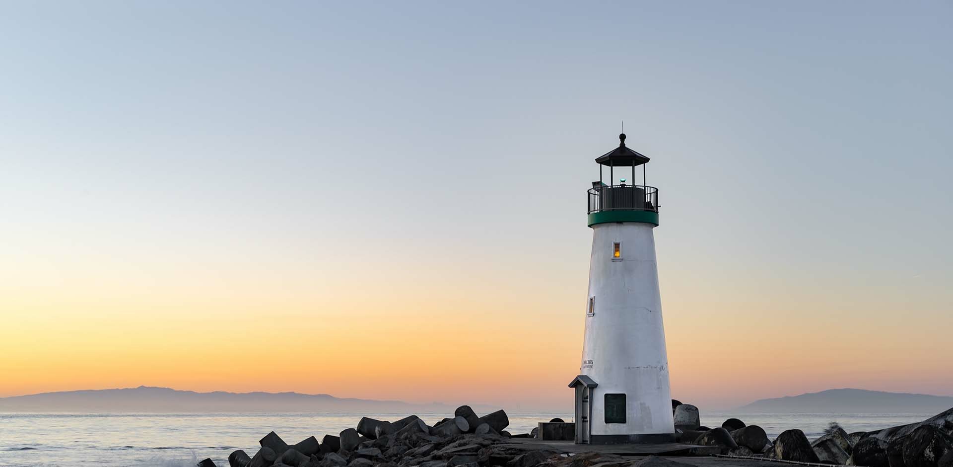 Leuchtturm auf einer Felsenküste mit Blick auf das Meer bei sanftem Sonnenuntergang.