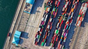 Farbig sortierte Containerreihen auf einem großen Hafengelände direkt am Wasser, Symbol für internationalen Warenverkehr.