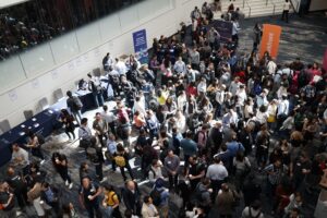 Zahlreiche Personen besuchen eine Konferenz oder Messe, tauschen sich an Ständen aus und vernetzen sich.