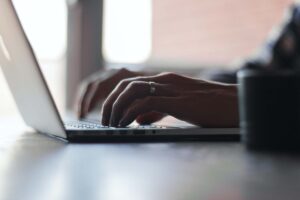 Eine Person tippt auf einem Laptop, Fokus auf den Händen und der Tastatur – Darstellung moderner Bildschirmarbeit.
