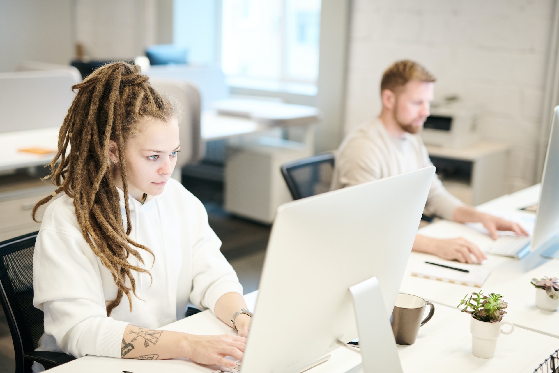 Zwei Personen arbeiten konzentriert an ihren Computern in einem hellen, modernen Büro.
