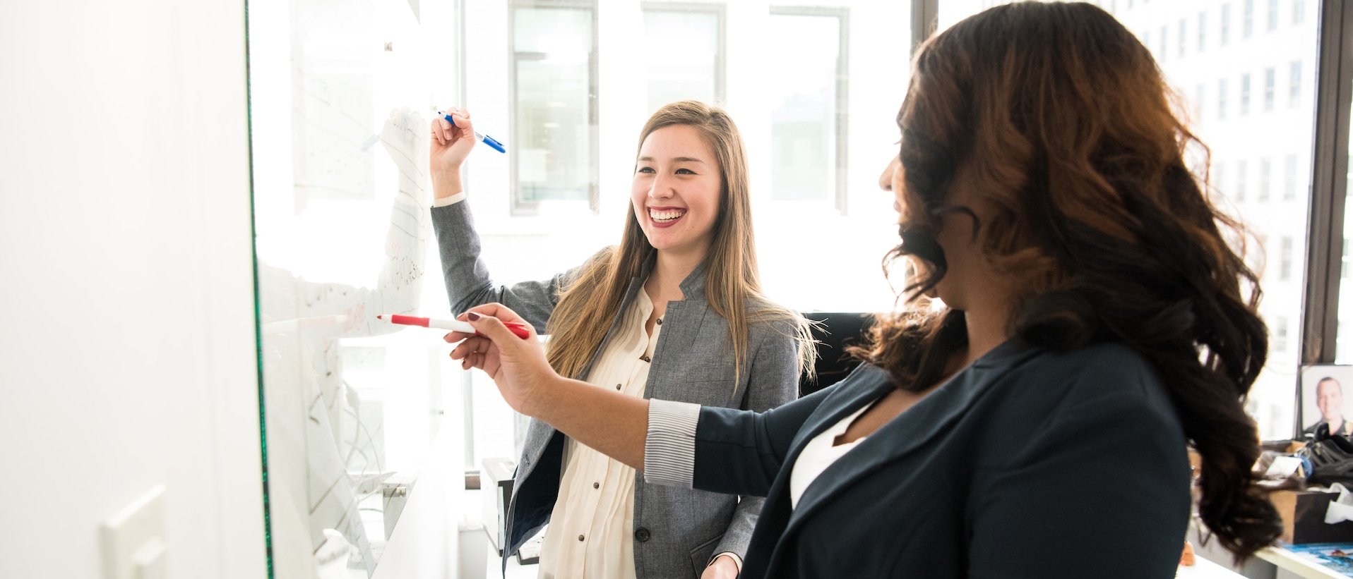 Zwei Personen planen gemeinsam an einem Whiteboard, lachen und tauschen sich in einem modernen Büro aus.